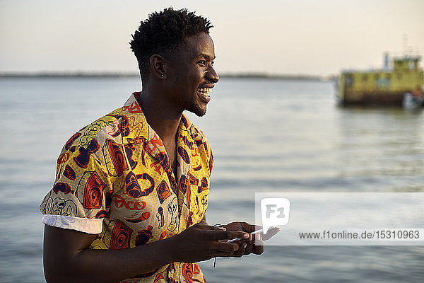 Young man standing at the sea  holding smartphone  portrait