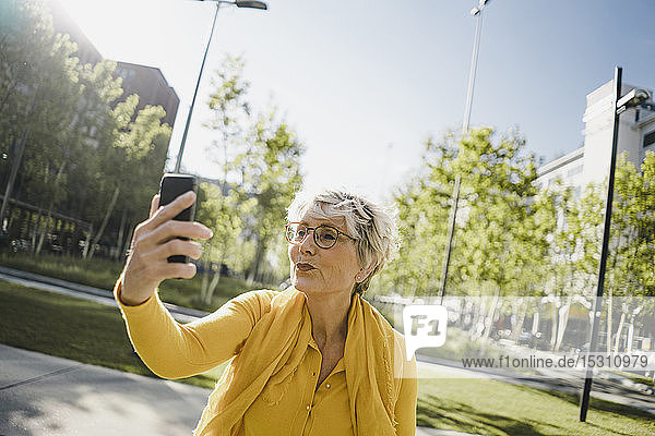 Porträt einer reifen Frau in gelber Kleidung  die mit Smartphone und schmollendem Mund Selbstgespräche führt