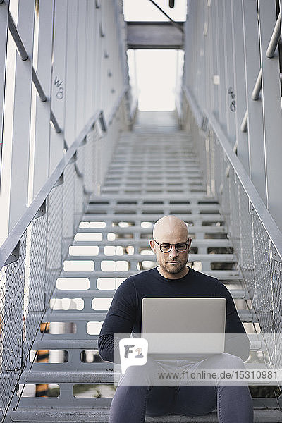 Portrait of bald man sitting on stairs using laptop