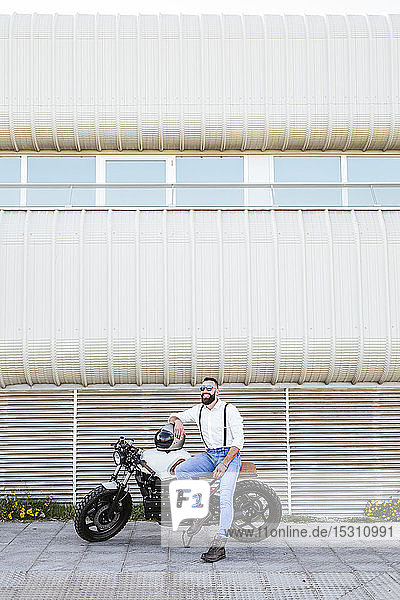 Bearded motorcyclist with mirrored sunglasses leaning on his motorbike