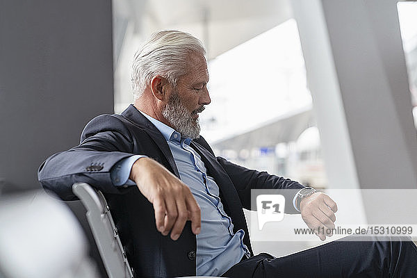 Mature businessman sitting in waiting area checking the time
