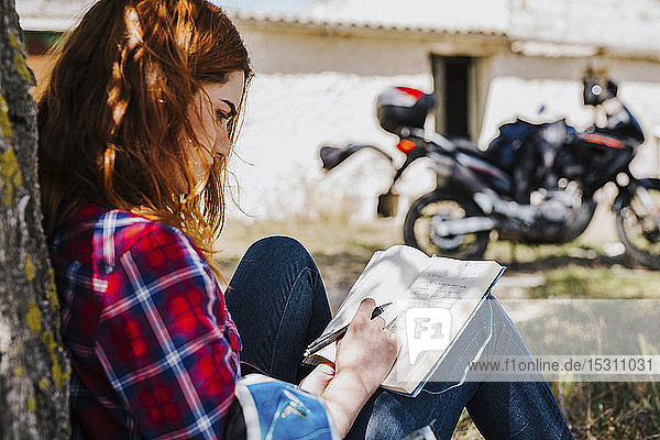 Redheaded motorcyclist leaning against tree trunk taking notes  Andalusia  Spain