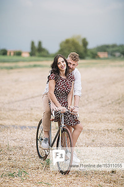 Portrait of couple on handcrafted racing cycle on stubble field