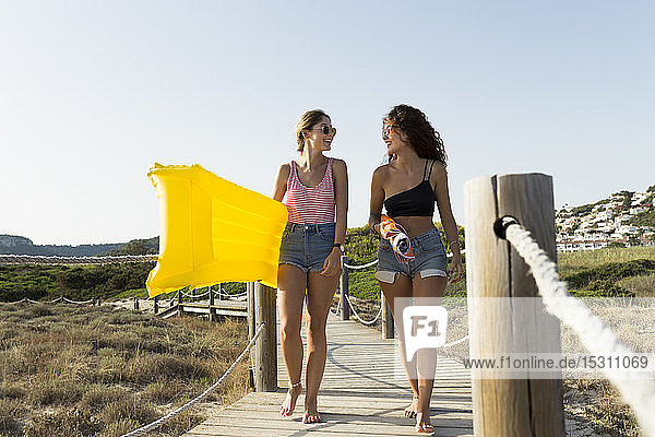 Junge Frauen mit gelber Luftmatratze und Sonnenschirm auf dem Weg zum Strand