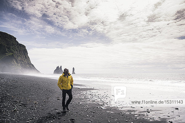 Erwachsener Mann geht an einem Lavastrand in Island