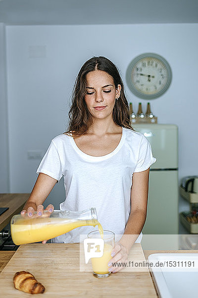 Junge Frau in der Küche gießt Orangensaft in Glas