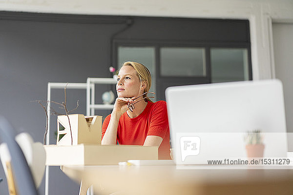 Junge Frau im Büro denkt mit Architekturmodell auf dem Schreibtisch