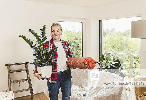 Woman moving into new home carrying carpet and potted plant