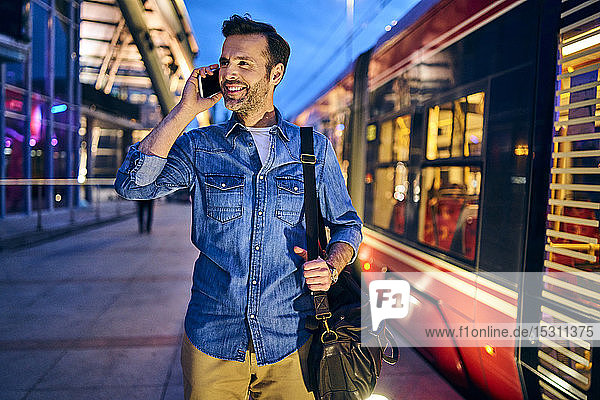 Mann telefoniert abends in der Stadt mit der Straßenbahn im Hintergrund