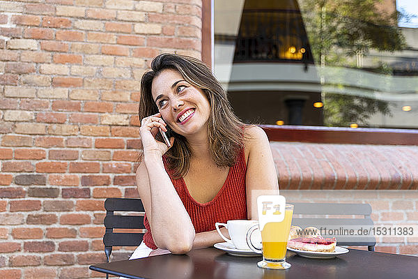 Porträt einer lächelnden jungen Frau  die in einem Straßencafé sitzt und telefoniert