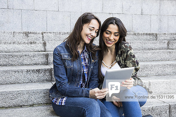 Happy young women watching tablet sitting on steps together in Madrid  Spain