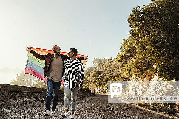 Homosexuelles Paar mit der Fahne Gay Pride geht auf einer Straße in den Bergen