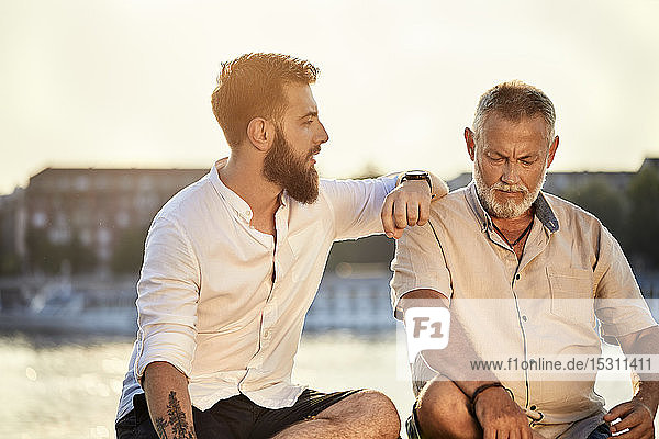 Father and adult son sitting on a wall at the riverside talking