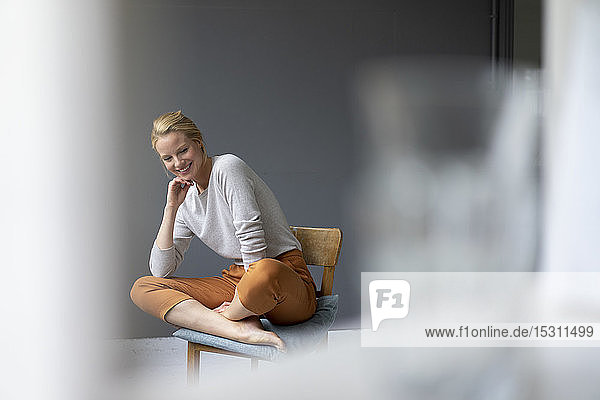 Lächelnde junge Frau sitzt im Büro auf einem Stuhl