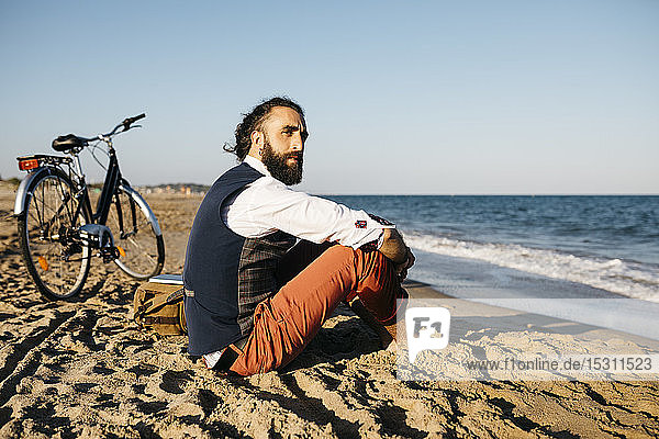 Well dressed man with his bike sitting on a beach