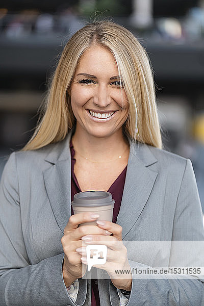 Porträt einer lächelnden blonden Geschäftsfrau mit Kaffee zum Mitnehmen