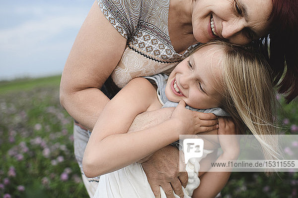 Glückliche Grossmutter umarmt Enkelin auf Blumenwiese