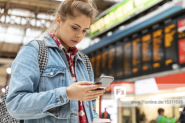 Junge Frau überprüft Smartphone am Bahnhof