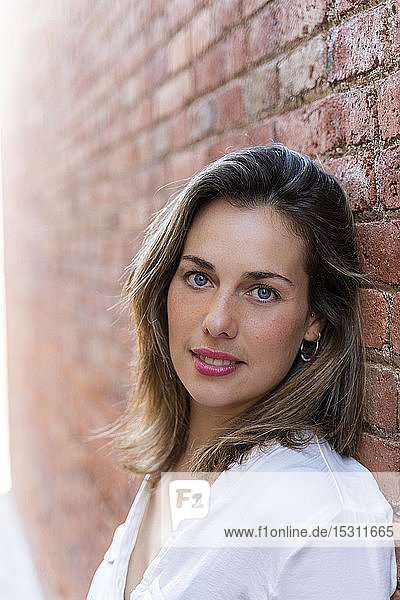 Portrait of smiling woman leaning on brick wall
