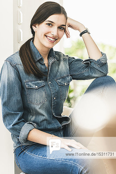 Porträt einer lächelnden jungen Frau  die zu Hause ein Jeanshemd trägt