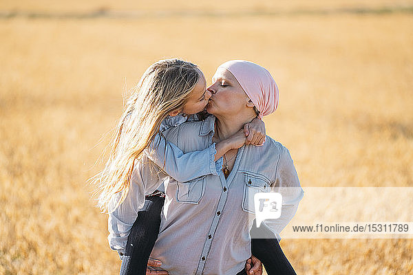 Eine Frau mit Krebs trägt ihre Tochter auf dem Rücken und küsst