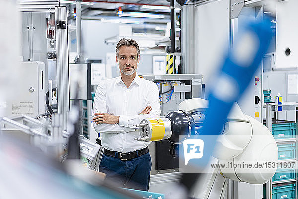 Portrait of confident businessman at assembly robot in a factory