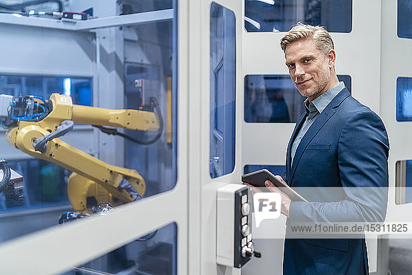 Portrait of a confident businessman in front of a robot in a modern factory