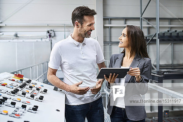 Geschäftsfrau und Angestellte unterhalten sich an einer Schalttafel in einer Fabrik