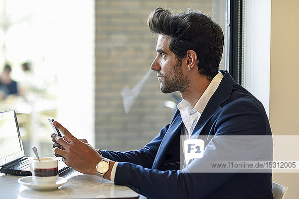 Businessman with smartphone and laptop in an urban cafe