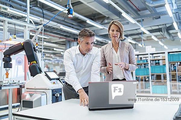 Businessman and businesswoman with laptop talking in a modern factory hall