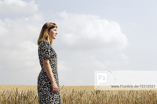 Young woman wearing dress with floral design standing in grain field