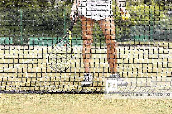 Beine der Tennisspielerin auf Rasenplatz durch das Netz gesehen