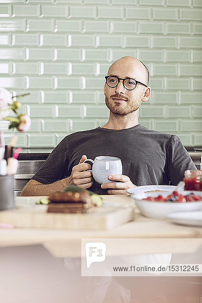 Mann  der zu Hause am Frühstückstisch sitzt und eine Tasse hält