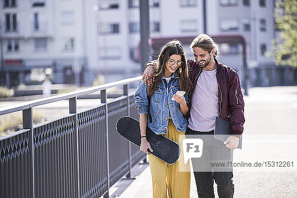 Junges Paar mit Skateboard und Smartphone auf einer Brücke