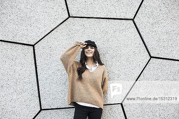Porträt einer lächelnden jungen Frau mit Mütze vor grauer Wand