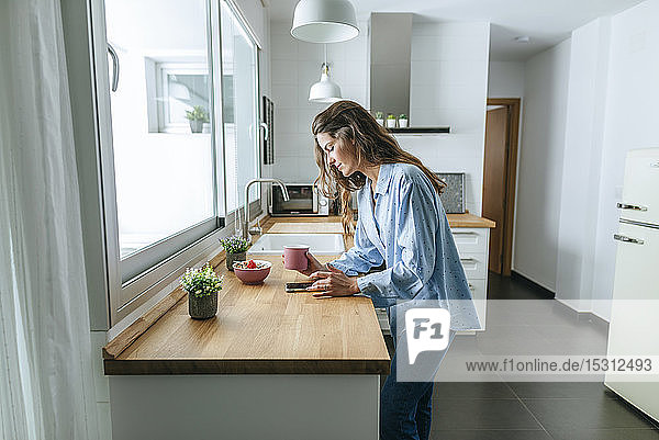 Young woman wearing pyjama in kitchen at home using cell phone