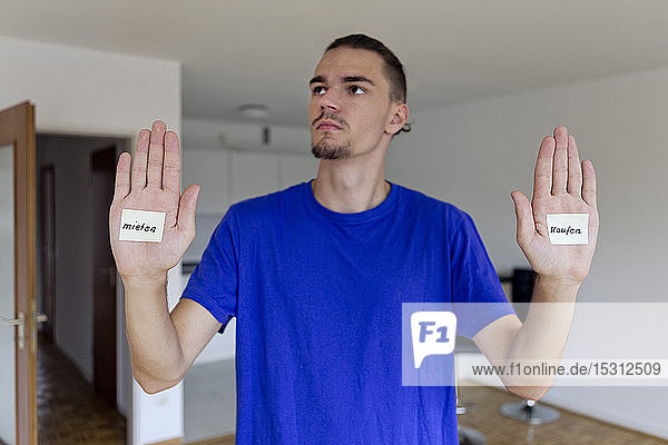 Young man in empty apartment with notes on the palms of his hands