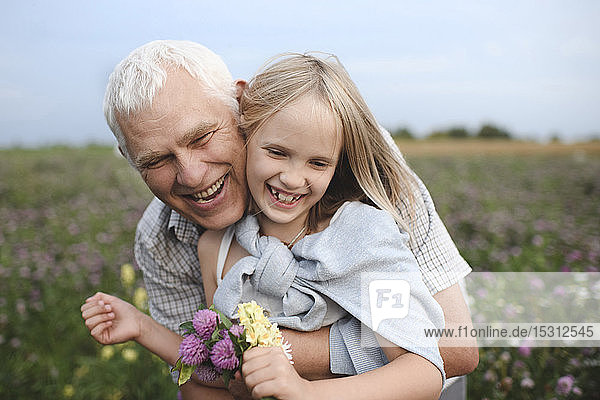 Portrait of happy grandfather and granddaughter with picked flowers on a meadow