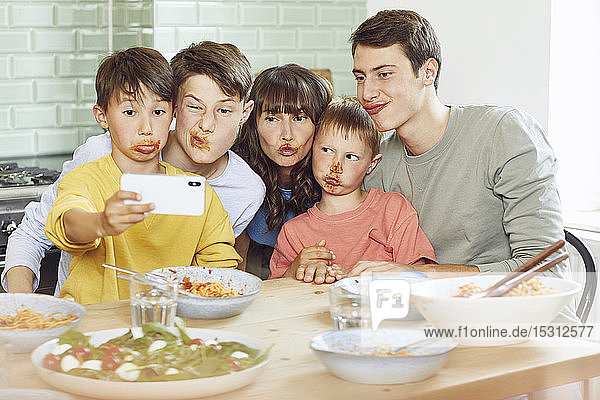 Mother and her four sons taking smartphone selfies at lunch  with faces full of tomato sauce