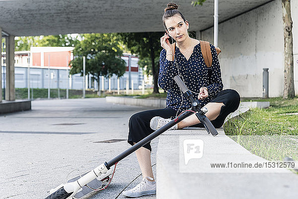 Young woman with electric scooterand earphones having a break
