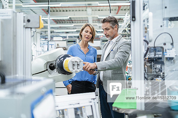 Businessman with tablet and woman talking at assembly robot in a factory