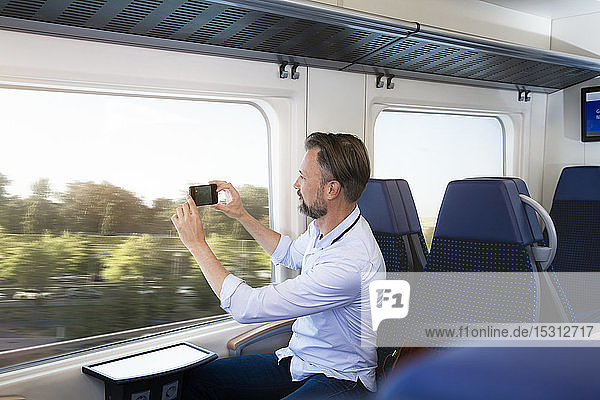 Mature man sitting in a train  taking pictures with his smartphone