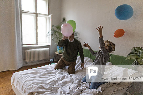 Happy grandfather and grandson playing with balloons on bed at home
