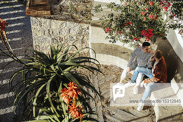 Homosexuelles Paar sitzt auf einer Stufe im Freien  umgeben von Blumen