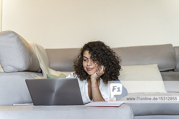 Young woman lying on couch at home using laptop