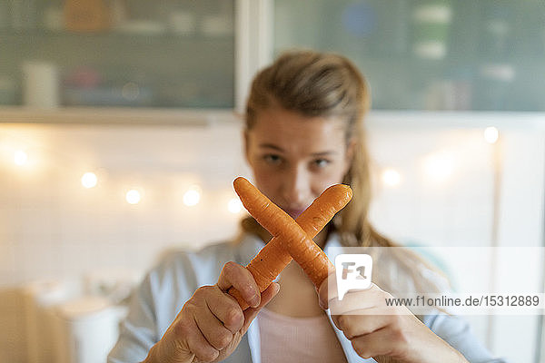 Young woman holding carrots at home