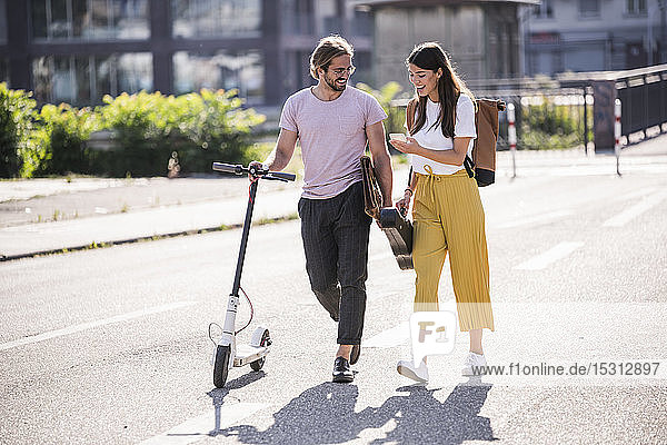 Young couple with electric scooter and smartphone walking on the street