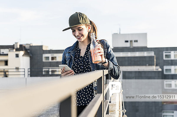 Smiling young woman with drink and cell phone on parking deck