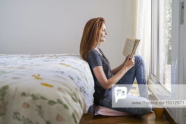 Junge Frau zu Hause chillt im Schlafzimmer und liest ein Buch