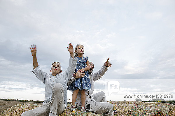 Father and his children sitting on hay bales  watching sky